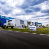 Blue Origin manufacturing facility exterior with large blue facade, landscaped grounds, and industrial coating system.
